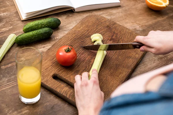 Cropped shot of woman cutting celery on wooden chopping board — Stock Photo