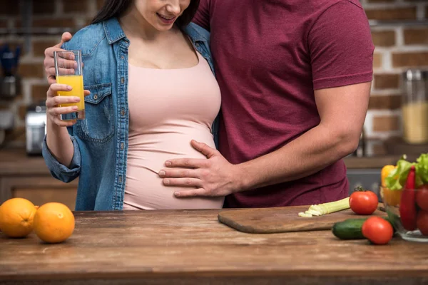 Обрізаний знімок людини, що торкається живота вагітної дружини, тримає склянку свіжого соку — стокове фото