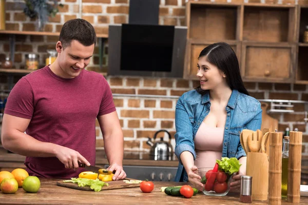 Happy young pregnant couple preparing fresh vegetable salad together — Stock Photo