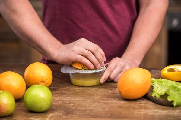 Обрезанный снимок молодого человека, выжимающего свежий апельсиновый сок дома — стоковое фото