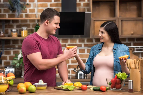Felice giovane coppia incinta spremendo succo fresco insieme a casa — Foto stock