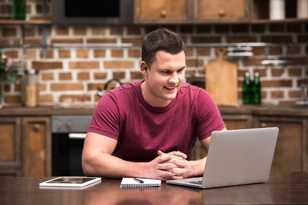 Lächelnder junger Mann bei der Arbeit zu Hause mit digitalen Geräten — Stockfoto