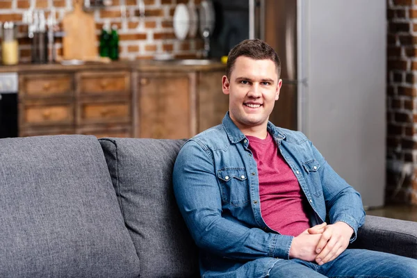 Handsome young man sitting on couch and smiling at camera — Stock Photo