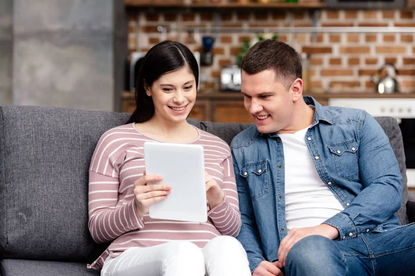 Sorrindo jovem casal grávida usando tablet digital juntos em casa — Fotografia de Stock