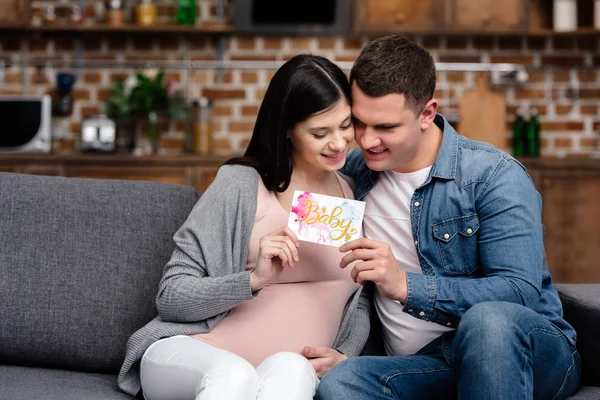Heureux jeune couple enceinte tenant la carte avec mot bébé — Photo de stock