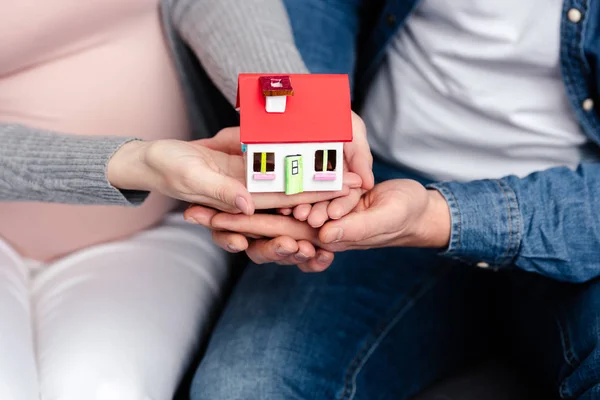 Close-up visão parcial de jovem casal grávida segurando modelo de casa pequena — Fotografia de Stock