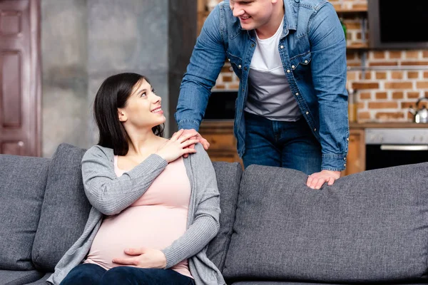 Обрізаний знімок щасливої молодої вагітної пари, посміхаючись один одному вдома — стокове фото