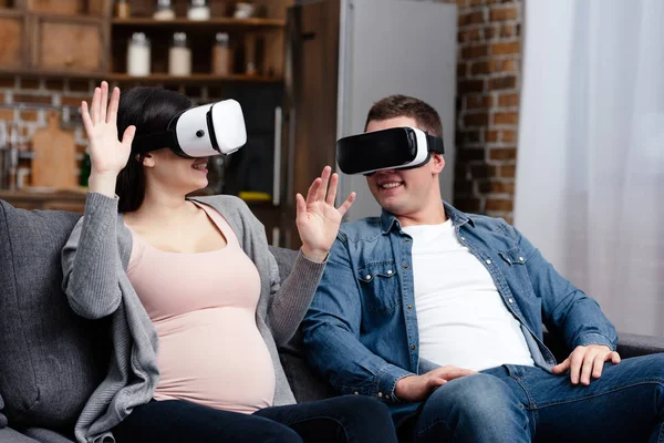 Felice giovane coppia incinta utilizzando cuffie realtà virtuale insieme a casa — Foto stock