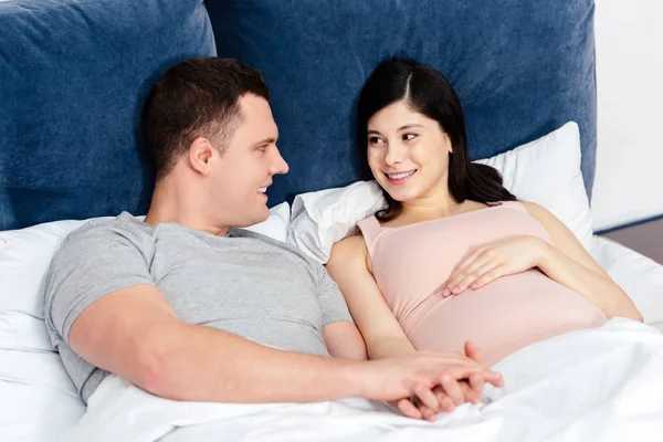 Heureux jeune couple enceinte couché ensemble dans le lit et se regardant — Photo de stock