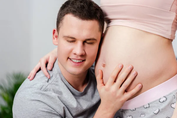 Обрізаний знімок щасливого чоловіка, що слухає живіт вагітної жінки — стокове фото