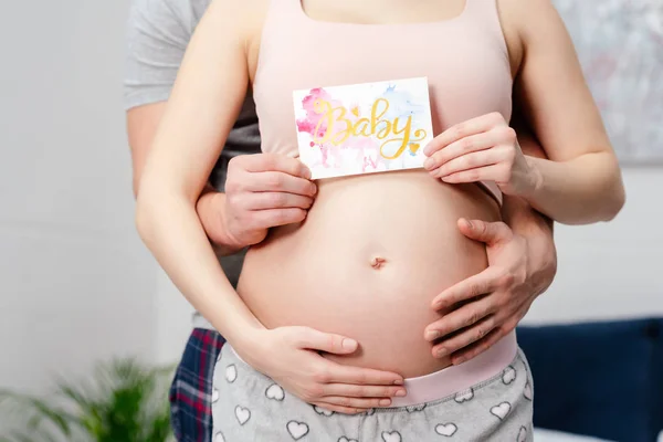 Tiro recortado de grávida casal segurando cartão com palavra bebê — Fotografia de Stock