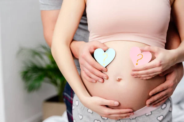 Cropped shot of man hugging pregnant woman and holding blue and pink hearts with question marks — Stock Photo