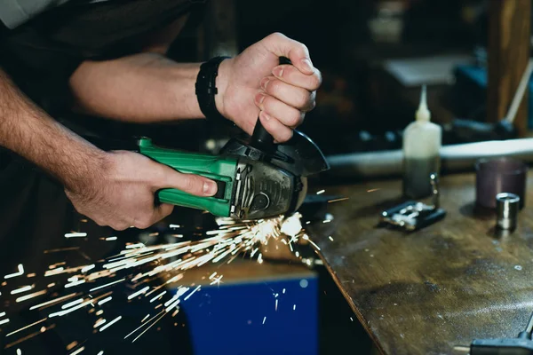 Nahaufnahme eines Mannes, der in der Werkstatt mit dem Winkelschleifer Metall schneidet — Stockfoto