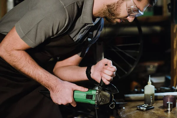 Erschossener Arbeiter mit Schutzbrille hält Winkelschleifer in Werkstatt — Stockfoto