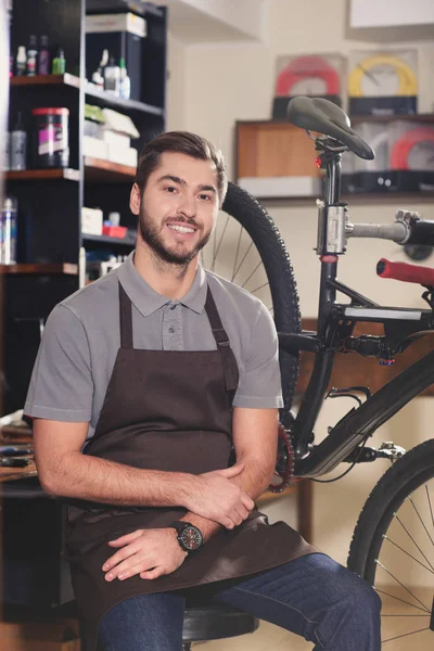 Handsome young repairman in apron smiling at camera in workshop — Stock Photo