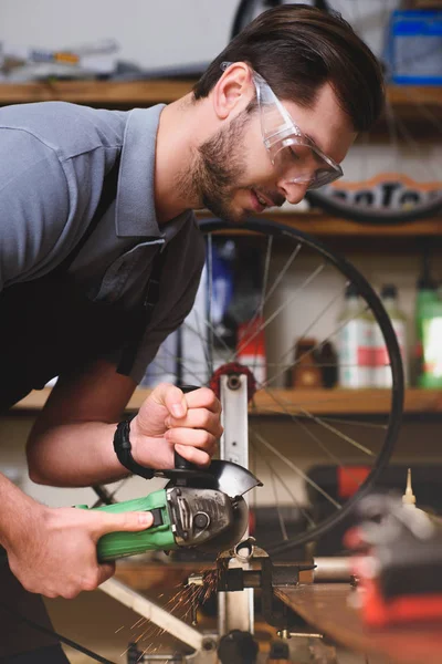 Молодой человек в защитных очках держит угловой станок в мастерской — стоковое фото