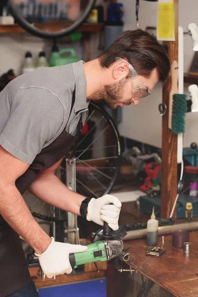 Side view of young repairman in protective workwear holding angle grinder in workshop — Stock Photo