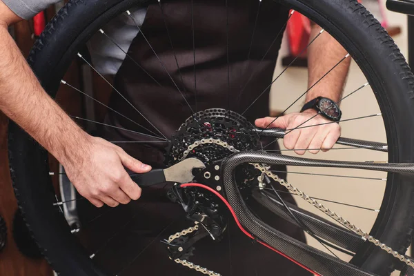 Cropped shot of man in apron fixing bicycle wheel and chain with wrench — Stock Photo