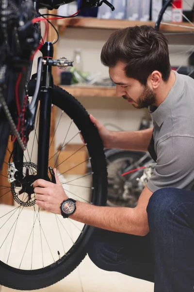 Young male worker in apron fixing bicycle in workshop — Stock Photo