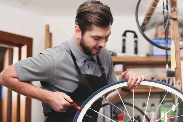 Jeune travailleur masculin dans tablier de fixation roue de vélo dans l'atelier — Photo de stock