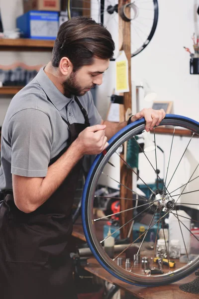 Jeune mécanicien dans tablier réparer roue de vélo dans l'atelier — Photo de stock