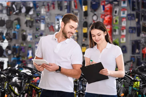 Smiling young managers working with clipboard and digital tablet in bicycle shop — Stock Photo