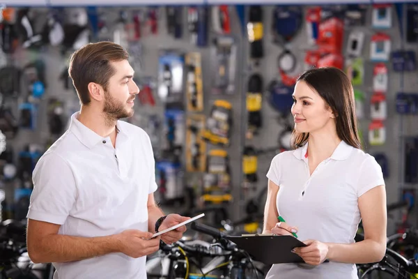 Smiling young workers with clipboard and digital tablet looking at each other in bike shop — Stock Photo