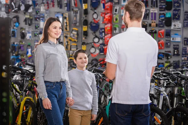 Вид ззаду продавця, дивиться на усміхнену матір і сина в велосипедному магазині — стокове фото