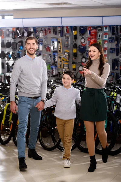Pais felizes com o pequeno filho fazendo compras juntos na loja de bicicletas — Fotografia de Stock