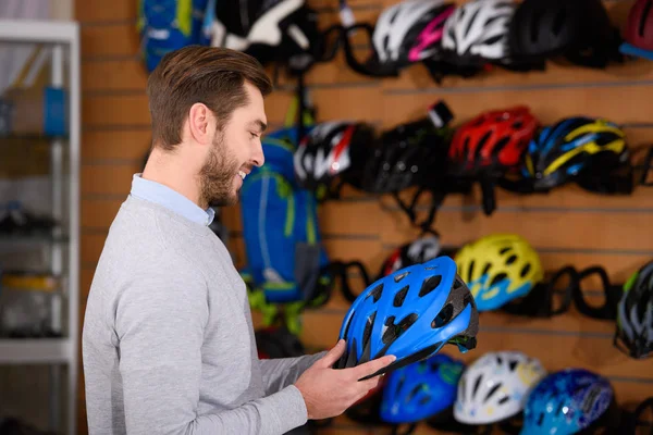 Sonriente joven sosteniendo casco de bicicleta en la tienda de bicicletas - foto de stock