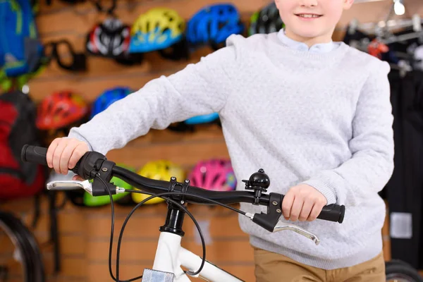 Cropped shot of smiling little boy standing with bicycle in bike shop — Stock Photo