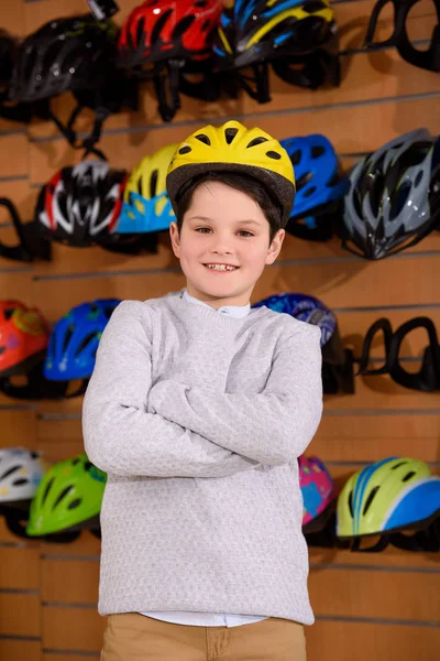Lindo niño pequeño con casco de bicicleta y sonriendo a la cámara en la tienda de bicicletas - foto de stock