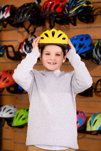 Cute little boy putting on bicycle helmet and smiling at camera in bike shop — Stock Photo