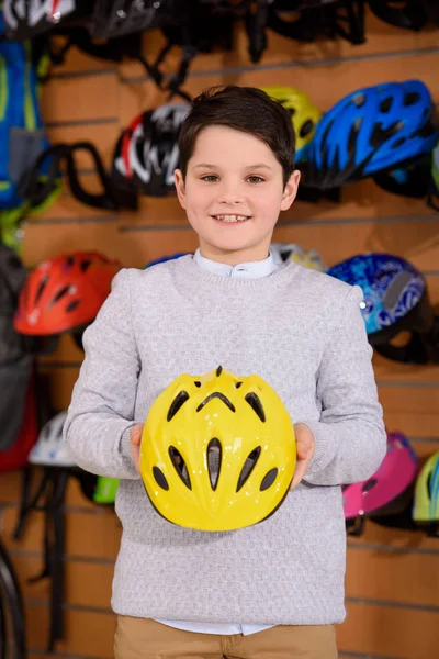 Cute little boy holding helmet and smiling at camera in bicycle shop — Stock Photo