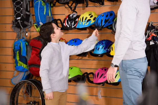 Recortado tiro de padre y sonriente hijo la elección de cascos de bicicleta en la tienda de bicicletas - foto de stock