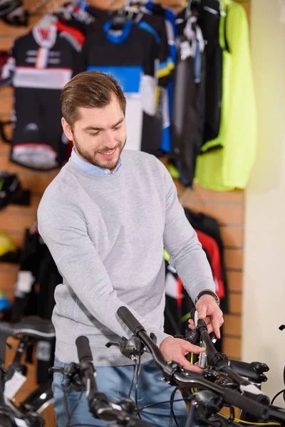 Smiling young man looking at bikes in bicycle shop — Stock Photo