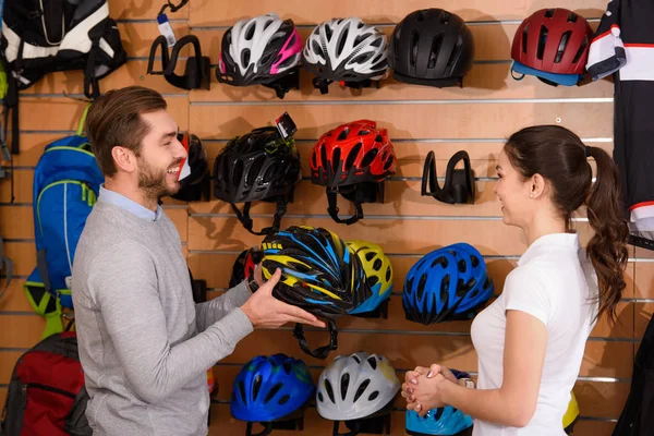 Side view of seller and customer looking at each other while choosing bicycle helmet in bike shop — Stock Photo