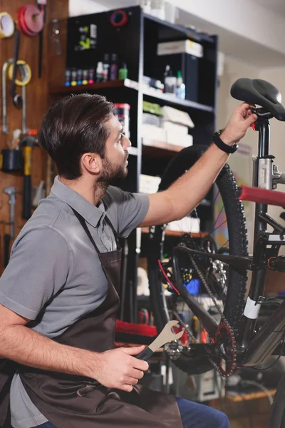 Joven reparador en delantal fijación bicicleta en taller - foto de stock
