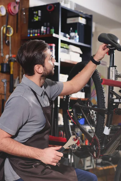 Young repairman in apron fixing bicycle in workshop — Stock Photo