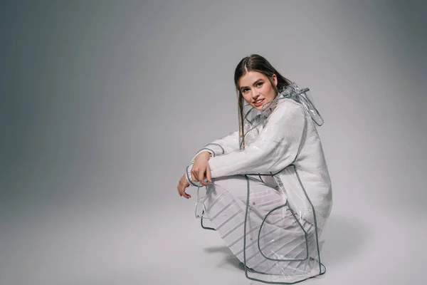 Elegante donna in impermeabile alla moda con occhiali da vista che guarda la fotocamera su sfondo grigio — Foto stock