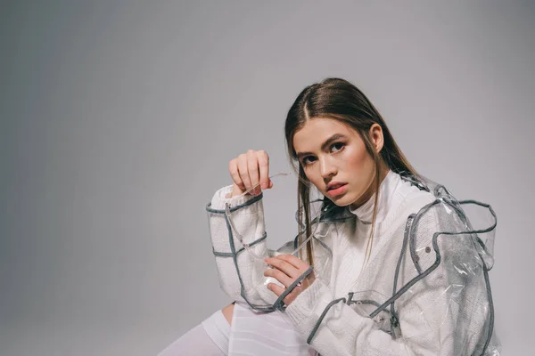 Portrait de femme élégante en imperméable à la mode avec des lunettes regardant la caméra sur fond gris — Photo de stock