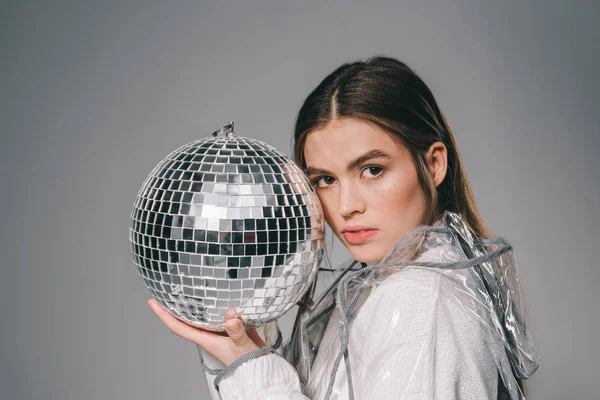 Retrato de mujer de moda con bola disco en las manos mirando a la cámara aislada en gris - foto de stock