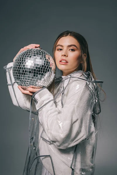 Retrato de mujer joven en impermeable de moda con bola disco aislado en gris - foto de stock