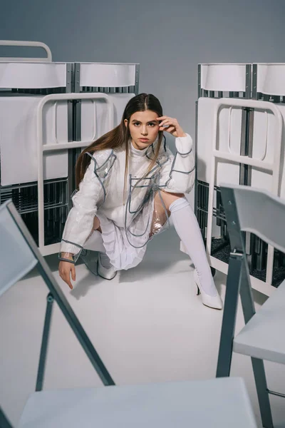 Mujer de moda en ropa blanca posando con sillas plegables detrás sobre fondo gris - foto de stock