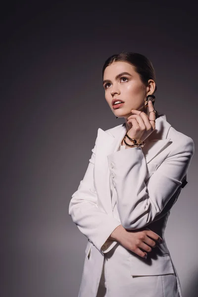 Retrato de mujer de moda pensativa en traje blanco mirando hacia otro lado en el fondo oscuro - foto de stock