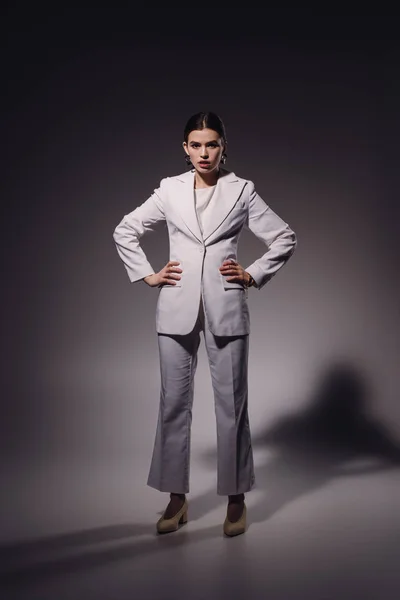 Joven mujer de moda akimbo en traje blanco posando sobre fondo oscuro - foto de stock