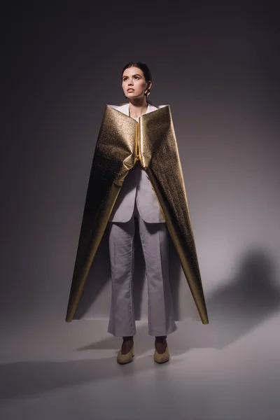 Mulher elegante em terno branco coberto de papel de embrulho dourado posando no fundo escuro — Fotografia de Stock