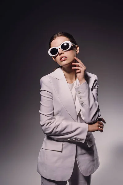 Portrait de femme élégante en costume blanc et lunettes posant sur fond sombre — Photo de stock