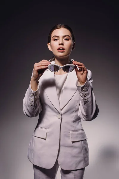 Portrait of stylish woman in white suit and eyeglasses posing on dark backdrop — Stock Photo