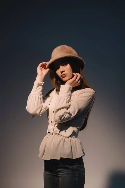 Retrato de hermosa mujer joven con ropa elegante y sombrero posando sobre fondo oscuro - foto de stock